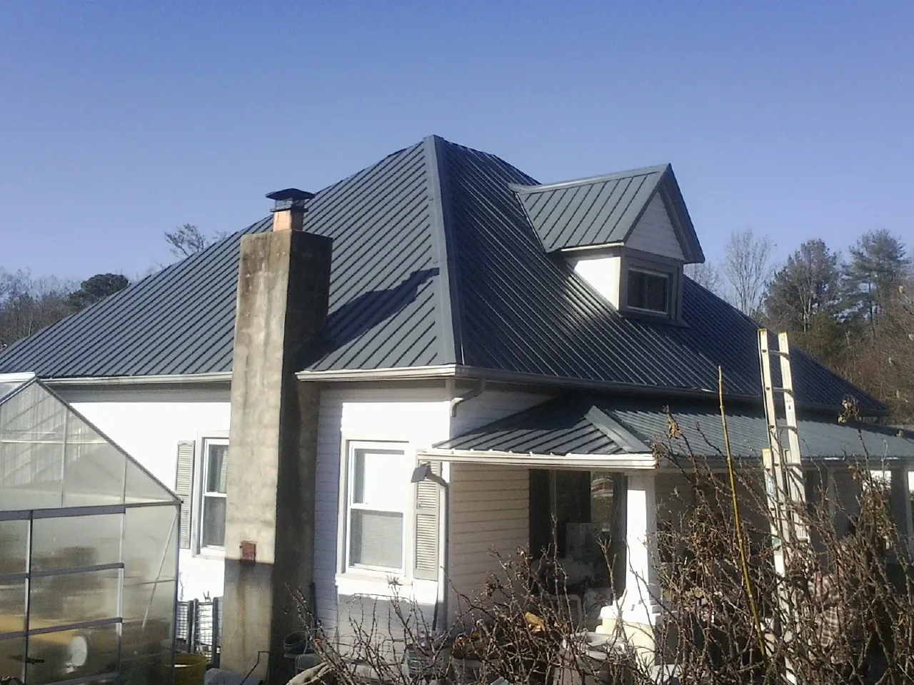 Dark blue standing seam metal roof on a white farmhouse with dormer — Slate & Tile Roof Repair by Roofing Brothers in Pinnacle