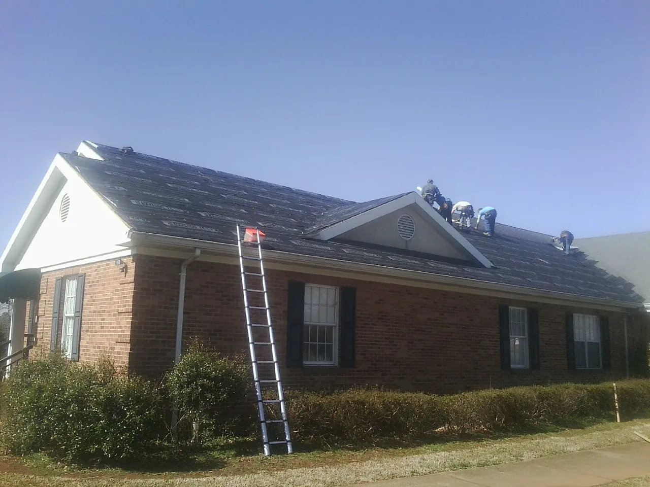 Crew tearing shingles off a brick ranch roof with a ladder set — Emergency Roof Repair work by our crew in Pinnacle
