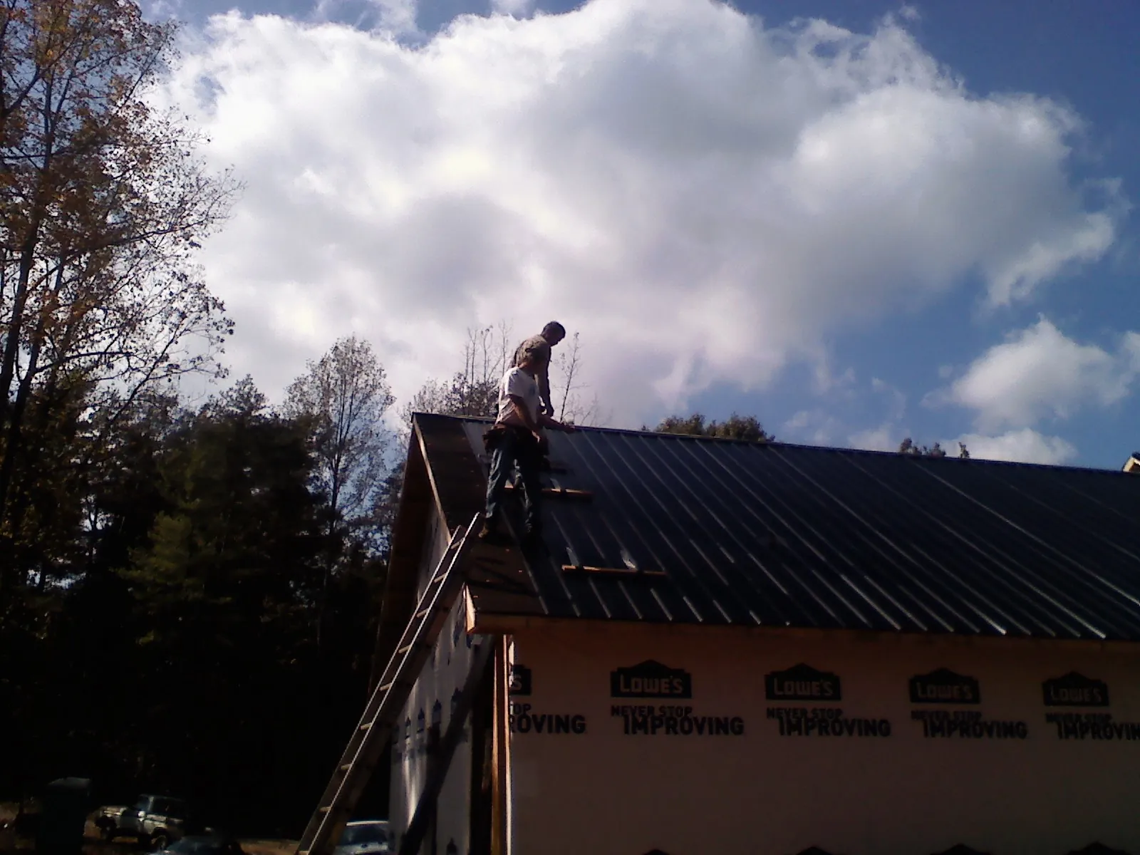Roofer fastening dark metal panels high against a cloudy sky, from a Roof Inspection job in Pinnacle
